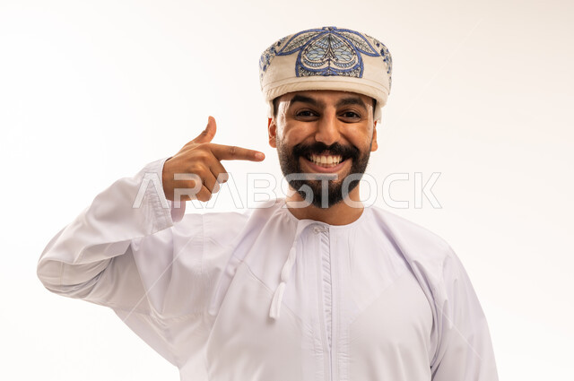 رجل عماني بالزي التقليدي يبتسم ويشير لوجهه