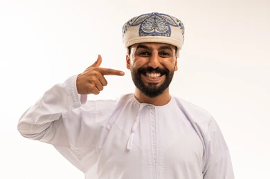 رجل عماني بالزي التقليدي يبتسم ويشير لوجهه