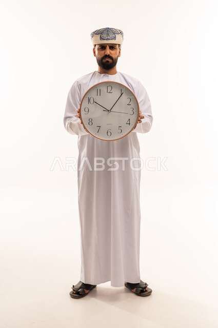 رجل عماني بالزي التقليدي يمسك ساعة حائط كبيرة