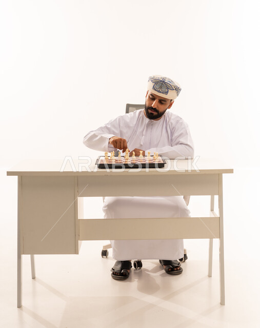 رجل عماني بالزي التقليدي يلعب الشطرنج خلف مكتب