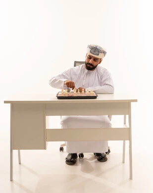 رجل عماني بالزي التقليدي يلعب الشطرنج خلف مكتب