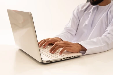 Omani Man Typing on Silver Laptop in White Dishdasha