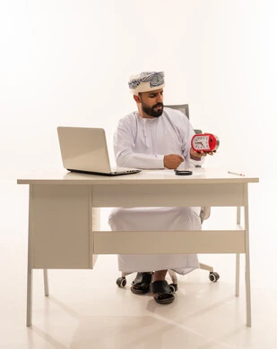 Omani Businessman with Alarm Clock at Office Desk