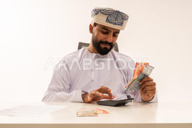 رجل عماني يستخدم الآلة الحاسبة مع العملات الورقية