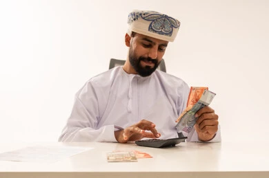 رجل عماني يستخدم الآلة الحاسبة مع العملات الورقية