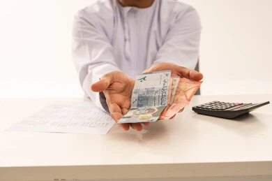 Omani Man Holding Omani Rial Banknotes at Office Desk