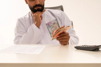 رجل عماني يمسك بالنقود وآلة حاسبة على مكتب العمل