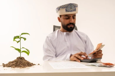 رجل عماني يحسب المال مع نبتة استثمار