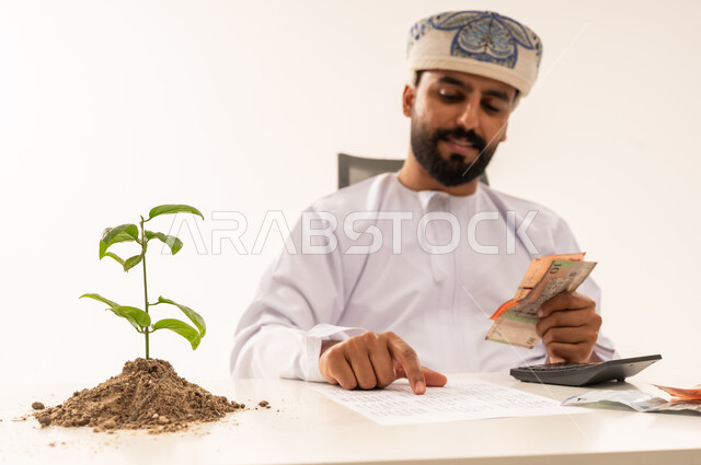 رجل عُماني يعد العملات النقدية مع نبتة نمو