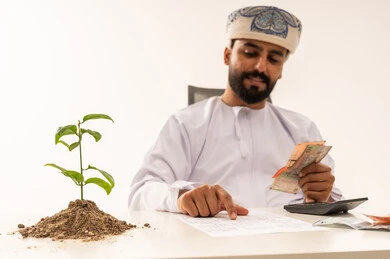 Omani Man Counting Rial Banknotes with Small Plant Omani Man Counting Rial Banknotes with Small Plant