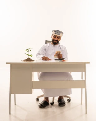 رجل عماني يعد الأموال على مكتب مع نبتة
