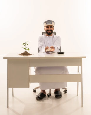 Omani Businessman Holding Money with Green Plant at Desk
