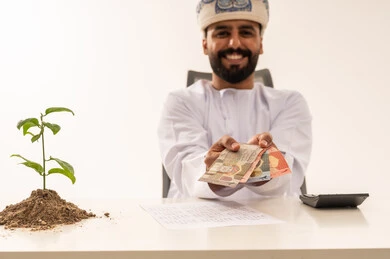 رجل عماني يحمل نقوداً ونبتة للاستثمار والنمو