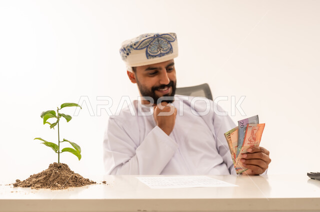 رجل عماني يحمل عملات ورقية بجانب شتلة نمو