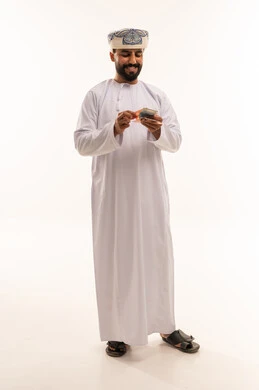 رجل عماني باللباس التقليدي يعد النقود الورقية