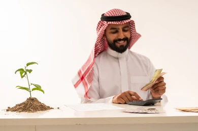 Saudi Businessman Counting Money Next to Growing Plant