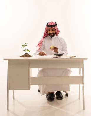 Saudi Businessman Holding Money with Green Plant on Desk