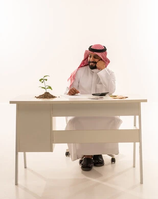 رجل أعمال سعودي مع نبتة خضراء على مكتبه