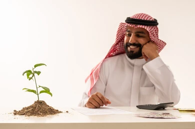 رجل أعمال سعودي يراقب نمو نبتة خضراء