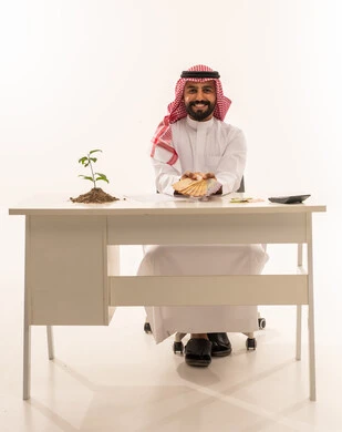 Saudi Man Holding Cash with Growth Plant at Desk