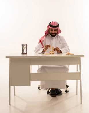 رجل سعودي على مكتب مع مكعبات خشبية وساعة رملية