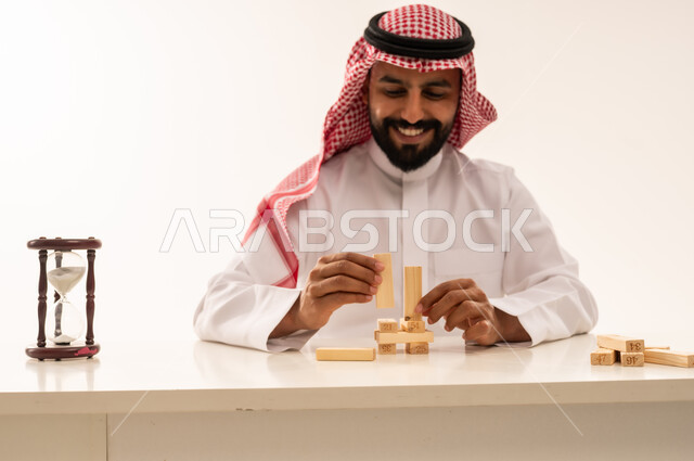 رجل سعودي يرص مكعبات خشبية مع ساعة رملية