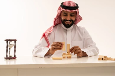 Saudi Man Stacking Wooden Blocks with Hourglass