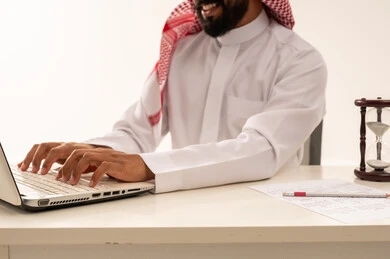 رجل أعمال سعودي يعمل على كمبيوتر محمول مع ساعة رملية