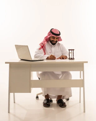 Saudi Businessman Writing at Office Desk with Laptop