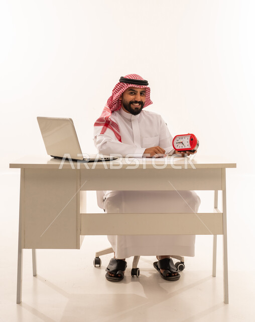 رجل سعودي يجلس خلف مكتب عمل ويمسك ساعة منبه