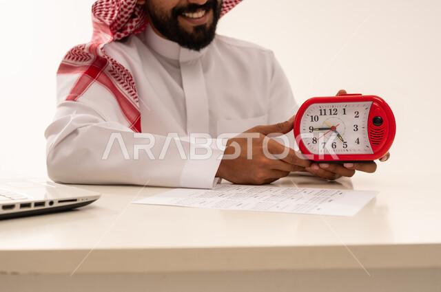 رجل سعودي يمسك ساعة منبه حمراء في المكتب