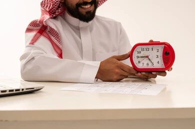 رجل سعودي يمسك ساعة منبه حمراء في المكتب