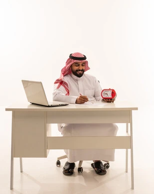 رجل أعمال سعودي على مكتب العمل مع ساعة منبه