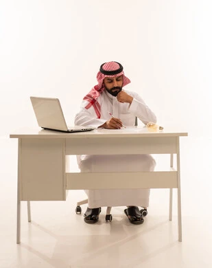 رجل أعمال سعودي يكتب على مكتب مع لابتوب