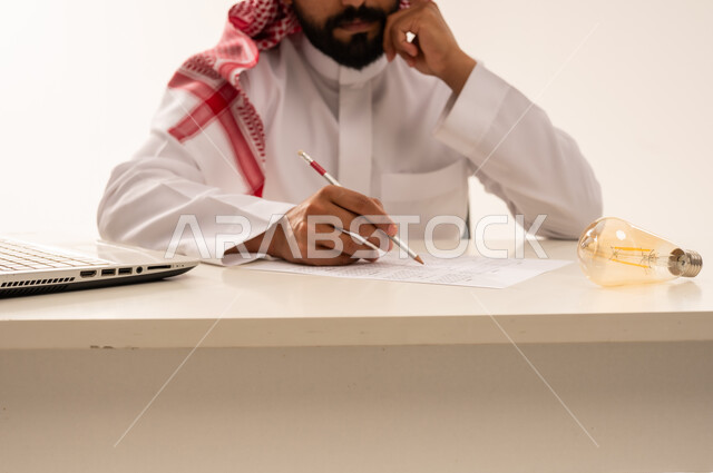 رجل سعودي يكتب على مكتب مع مصباح كهربائي