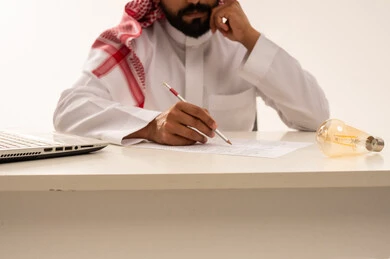 Saudi Man Writing at Office Desk with Light Bulb