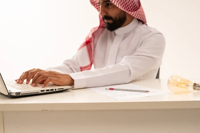 رجل سعودي يعمل على الكمبيوتر المحمول بالزي الرسمي
