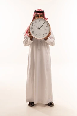 رجل سعودي يمسك ساعة حائط على خلفية بيضاء