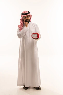 رجل سعودي بالثوب التقليدي يفكر مع ساعة منبه حمراء