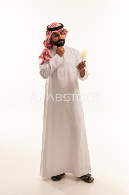 رجل سعودي بالثوب يفكر ويحمل مصباح كهربائي