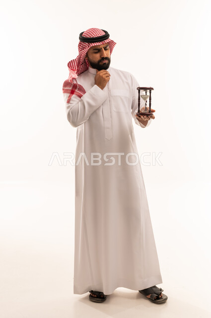 رجل سعودي يمسك ساعة رملية بخلفية بيضاء