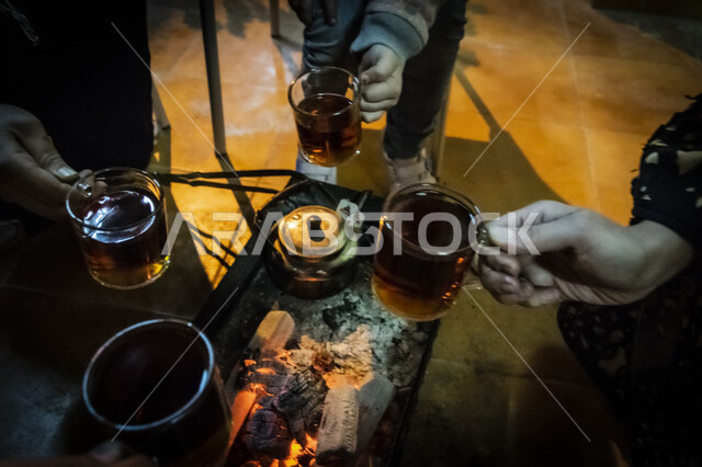 عائلة عربية خليجية سعودية، جلسة عائلية امام كانون التدفئة، الامساك بأكواب الشاي، تسخين المشروبات، حطب مشتعل، أجواء شتوية عائلية