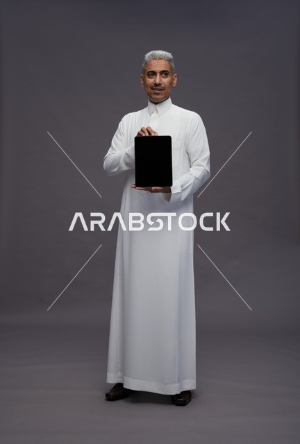 رجل سعودي بالثوب يمسك بجهاز لوحي