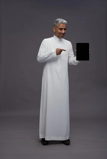 رجل سعودي بالثوب يشير إلى شاشة جهاز لوحي في الاستوديو