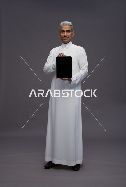رجل سعودي يحمل جهاز لوحي شاشة سوداء في استوديو