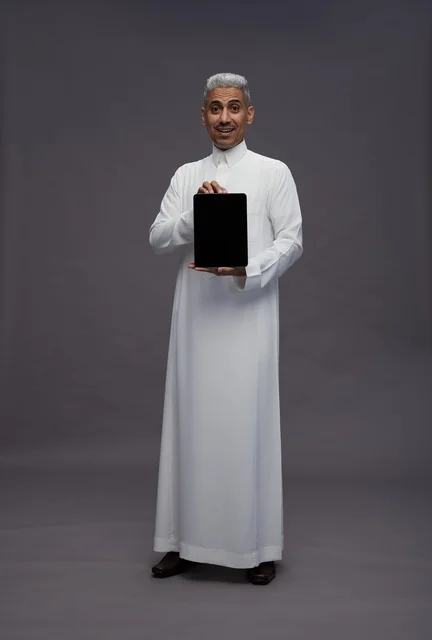 رجل سعودي يحمل جهاز لوحي أمام خلفية رمادية