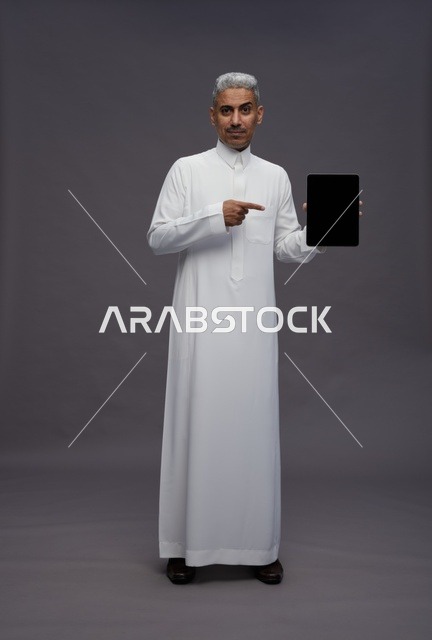 رجل سعودي بالثوب يشير إلى جهاز لوحي في الاستوديو