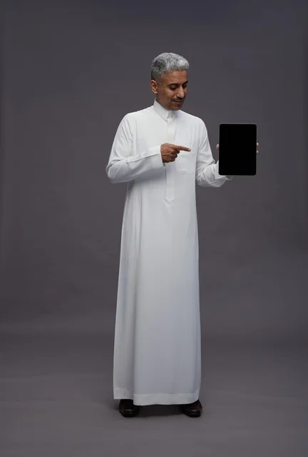 رجل سعودي يشير إلى جهاز لوحي أمام خلفية رمادية