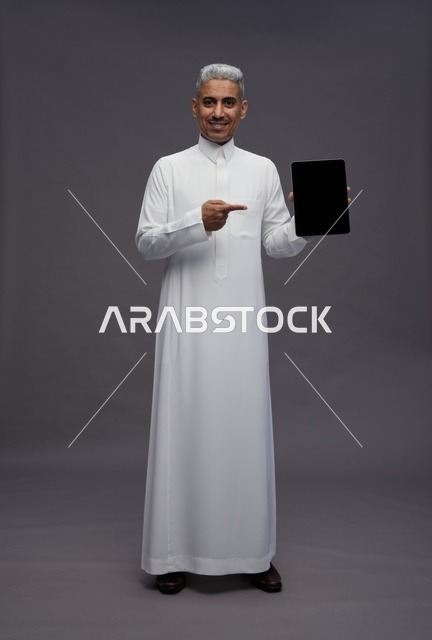 رجل سعودي بالثوب الأبيض يشير إلى شاشة جهاز لوحي