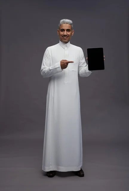 رجل سعودي بالثوب الأبيض يشير إلى شاشة جهاز لوحي
